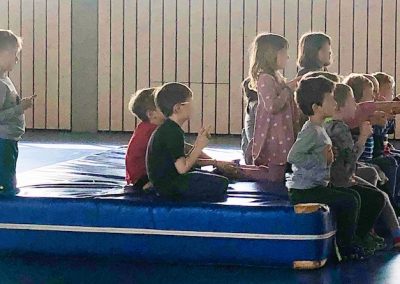 Kinder sitzen auf Weichbodenmatte und lauschen gespannt einer Geschichte zum Thema Selbstverteidigung